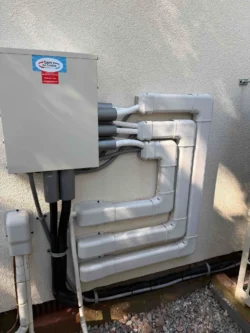 Four neatly organized white conduit pipes run from an electrical box mounted on a wall, each making angled turns and connected to black pipes below.