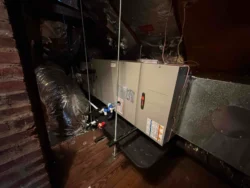 An HVAC unit installed in an attic, with insulated air ducts, metal supports, and a drip pan beneath the system.